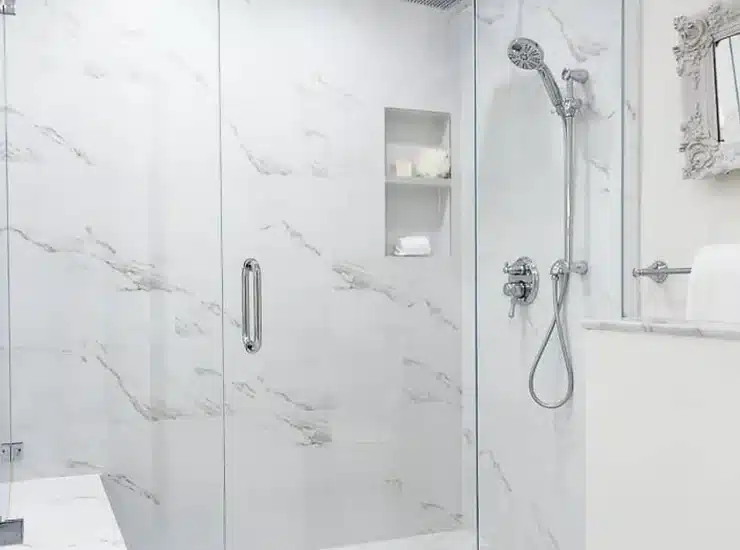 A modern, spacious bathroom featuring a glass-enclosed shower with a marble interior, a mounted showerhead, built-in shelving, and a bench. The area is well-lit with recessed lighting.