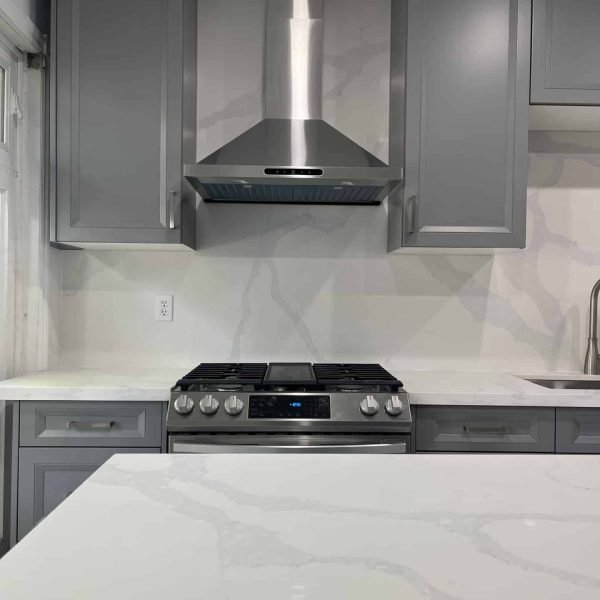 Sleek modern kitchen with white cabinets, a large island with quartz countertops, and built-in stainless steel appliances.