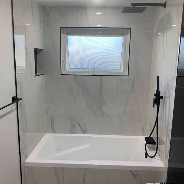 Drop in bathtub shower with black shower fixtures and shower niche